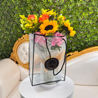 Bouquet of flowers in a clear bag on a white pedestal with a decorative chair and greenery in the background