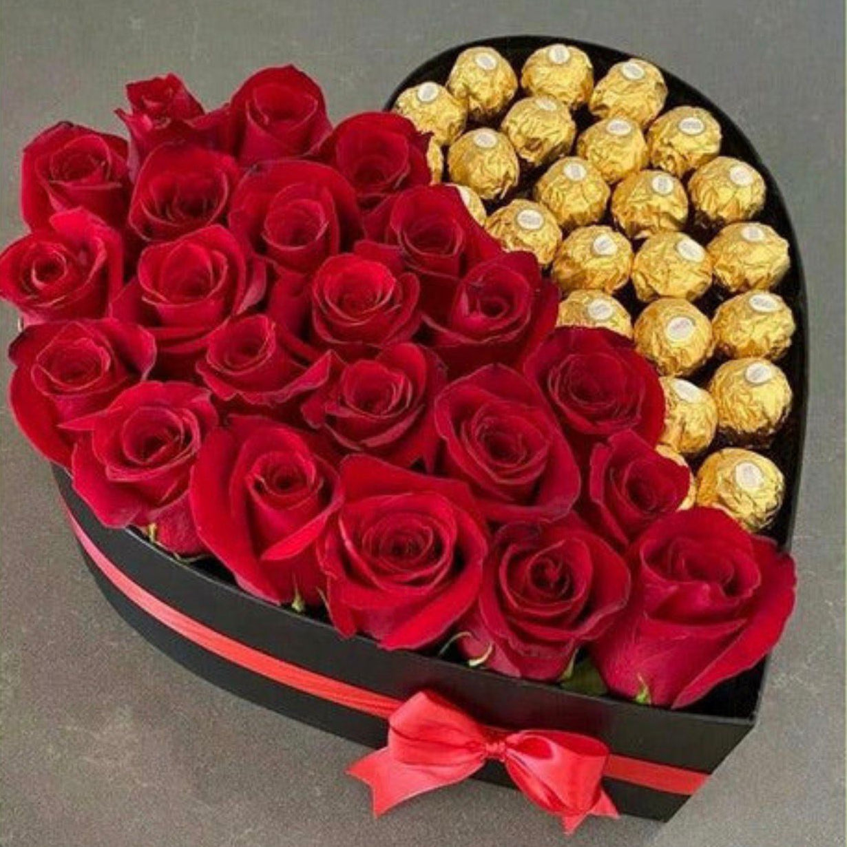 Heart-shaped box with red roses and gold Ferrero Rocher chocolates on a gray background