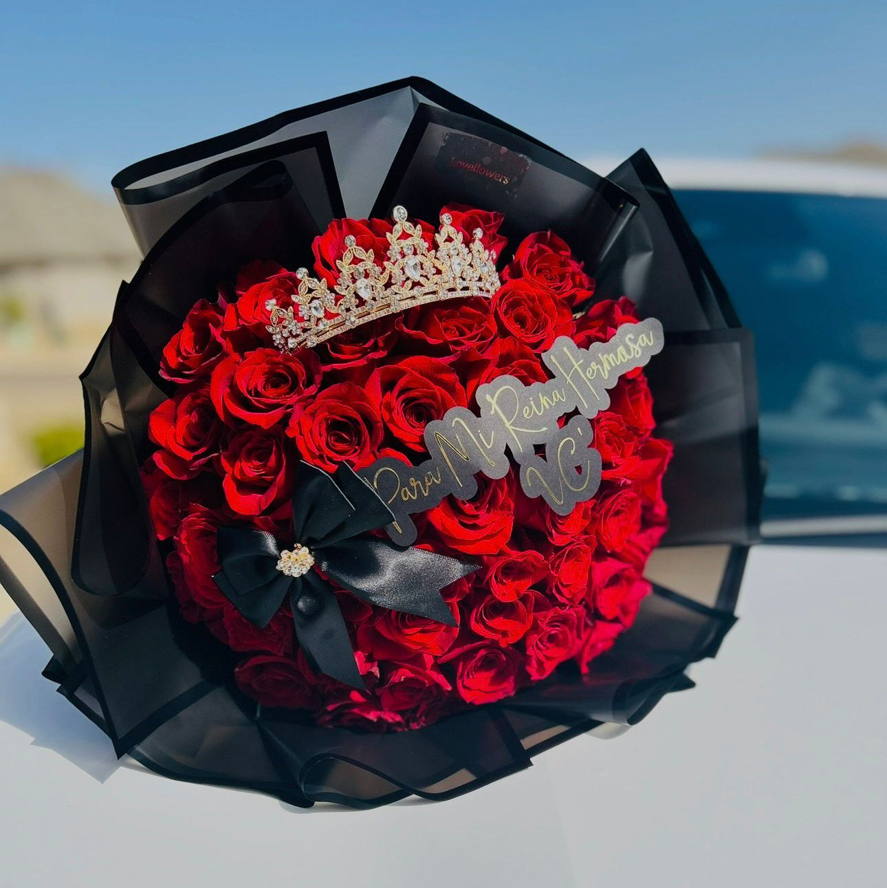 Bouquet of red roses with a tiara and 'I Do' rings on a car hood.
