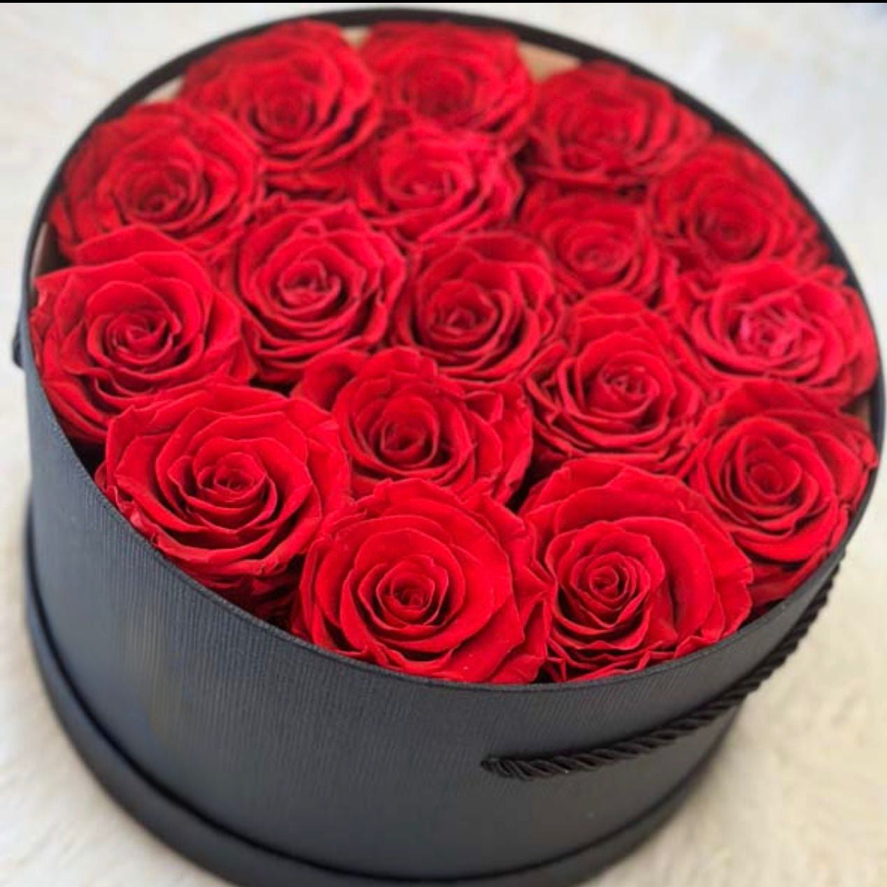 Black round box filled with red roses on a light background